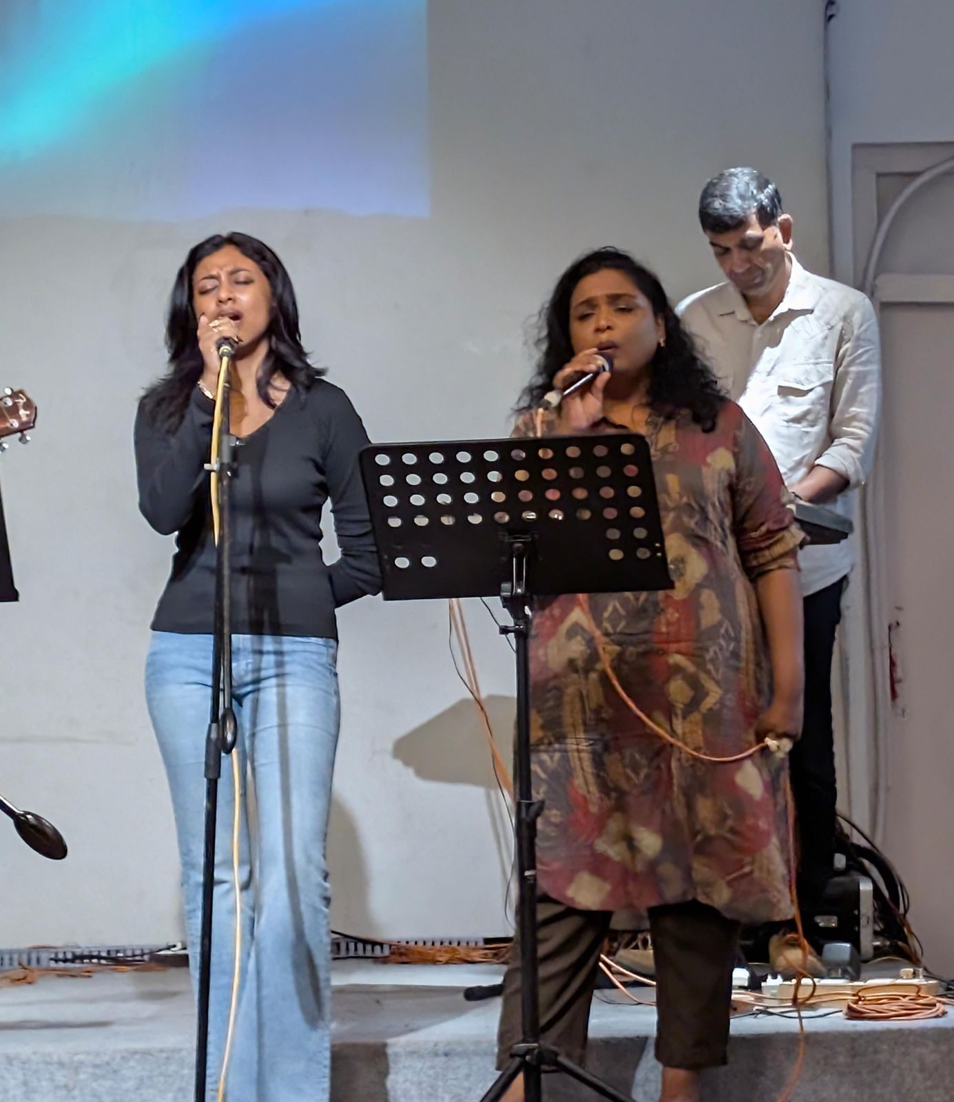 Two vocalists leading worship, with keys behind